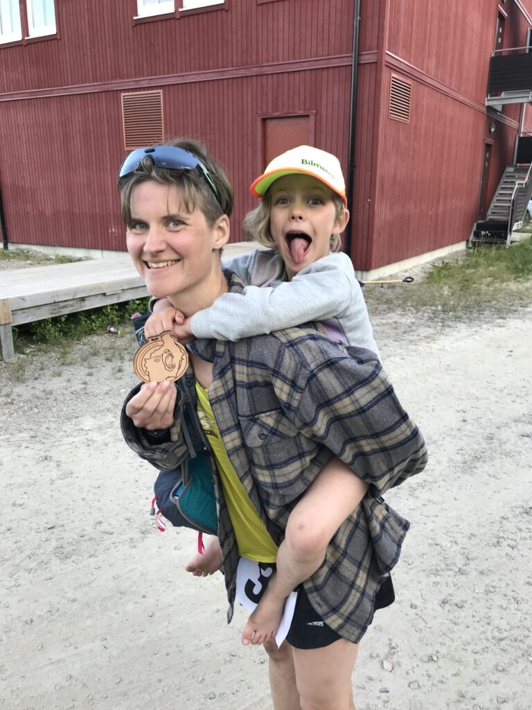 Lisa Kriga med dottern på ryggen, håller upp medaljen för Björnfrossa Ultramarathon
